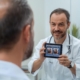 A doctor showing a middle-aged man before-and-after images of a hair transplant on a tablet, discussing treatment for a receding hairline after age 40.