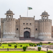 Lahore Fort main entrance with Pakistan flag, historic Mughal architecture, and landscaped gardens.