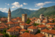 Scenic view of a historic Balkan city with red-roofed houses, medieval architecture, and mountains in the backdrop, representing the beauty of Balkan cities.