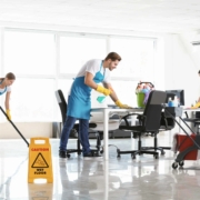 Professional cleaners providing Office Clean Out Services Kent WA in a modern, bright office space with cleaning supplies, vacuums, and "Wet Floor" signage.