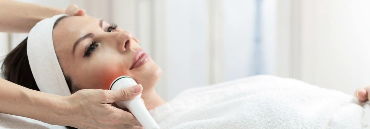 Woman receiving a professional skin tightening facial near Tysons Corner using a handheld device in a spa setting.